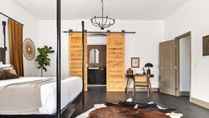 A bedroom with a bed, a desk, a chair, a cowhide rug, a mirror, and a sliding barn door. - Pueblo Villa - Sleeps 12 • 2 Homes on 2.5 Acres (Joshua Tree)