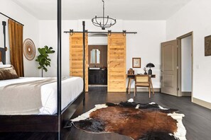 Slaapkamer met een bed, een bureau, een stoel, een kussen van runderleer, een spiegel en een schuifdeur in boerderijstijl.