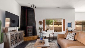 A living room with a fireplace, a sofa, a coffee table, and a TV. - Pueblo Villa - Sleeps 12 • 2 Homes on 2.5 Acres (Joshua Tree)