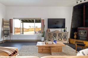 Een woonkamer met een grote televisie, houten meubels, een open haard en uitzicht op de omgeving.