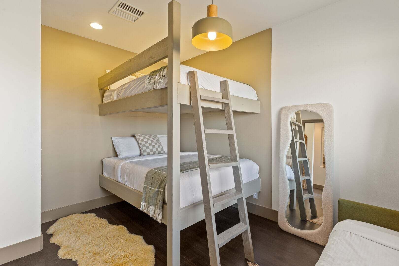 A bunk bed with a ladder, a mirror, and a fluffy rug in a room with a light fixture.