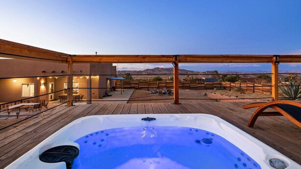 A hot tub on a wooden deck with a view of a building and mountains in the background. - Pueblo Villa - Sleeps 12 • 2 Homes on 2.5 Acres (Joshua Tree)