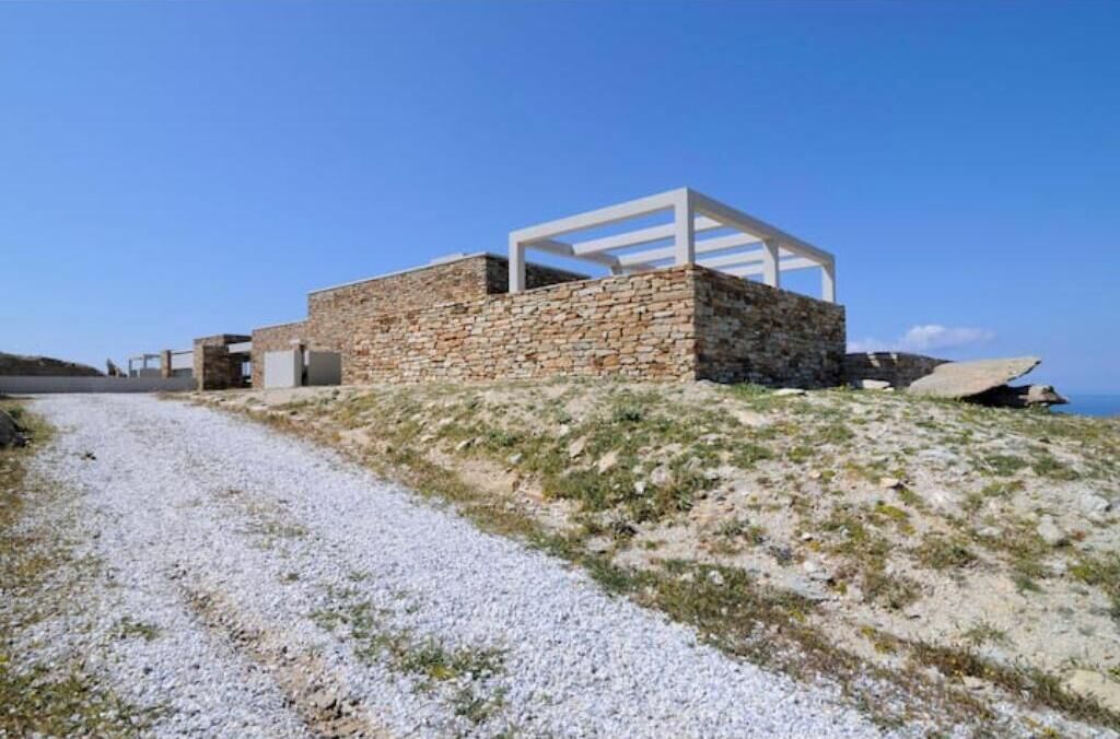 Een modern stenen gebouw met een witte structuur, gelegen aan een grindpad met uitzicht op zee.