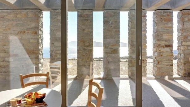 Una stanza con pilastri in pietra, un tavolo con sedie e vista sul mare.