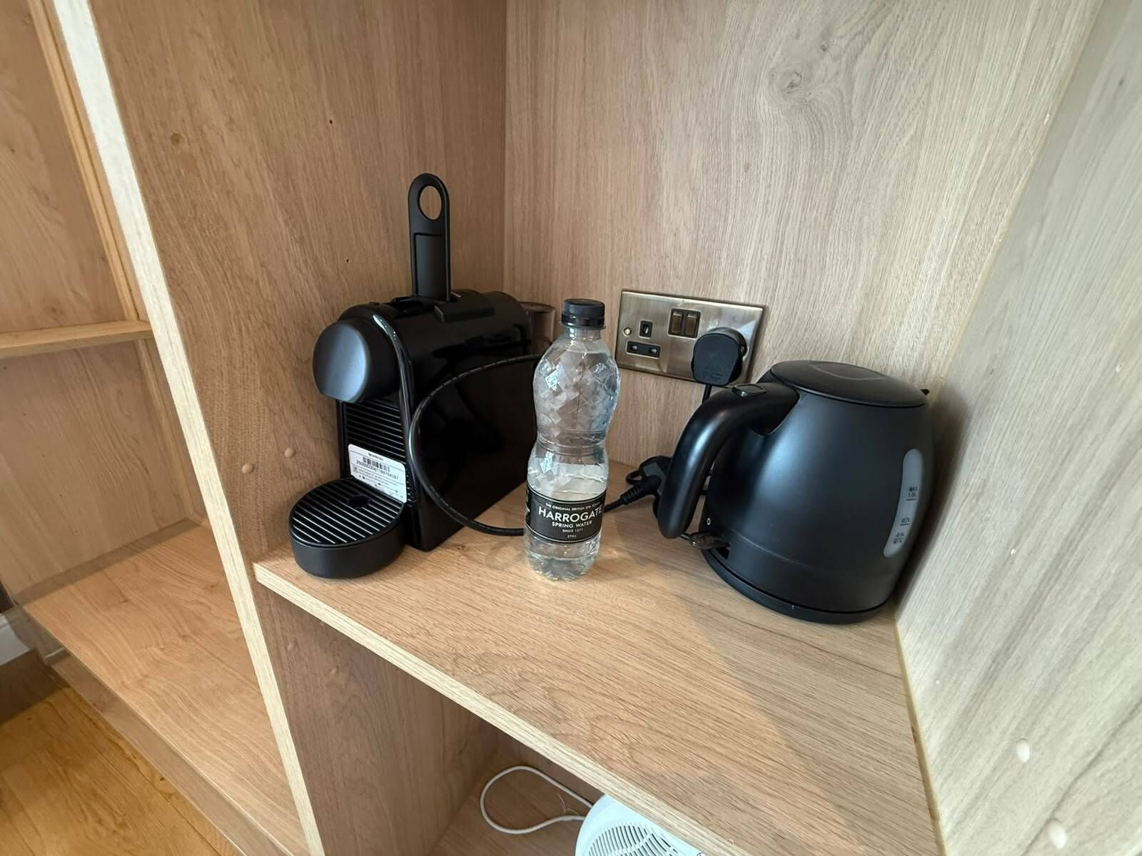 A wooden shelf with a black coffee maker, a water bottle, and a kettle.