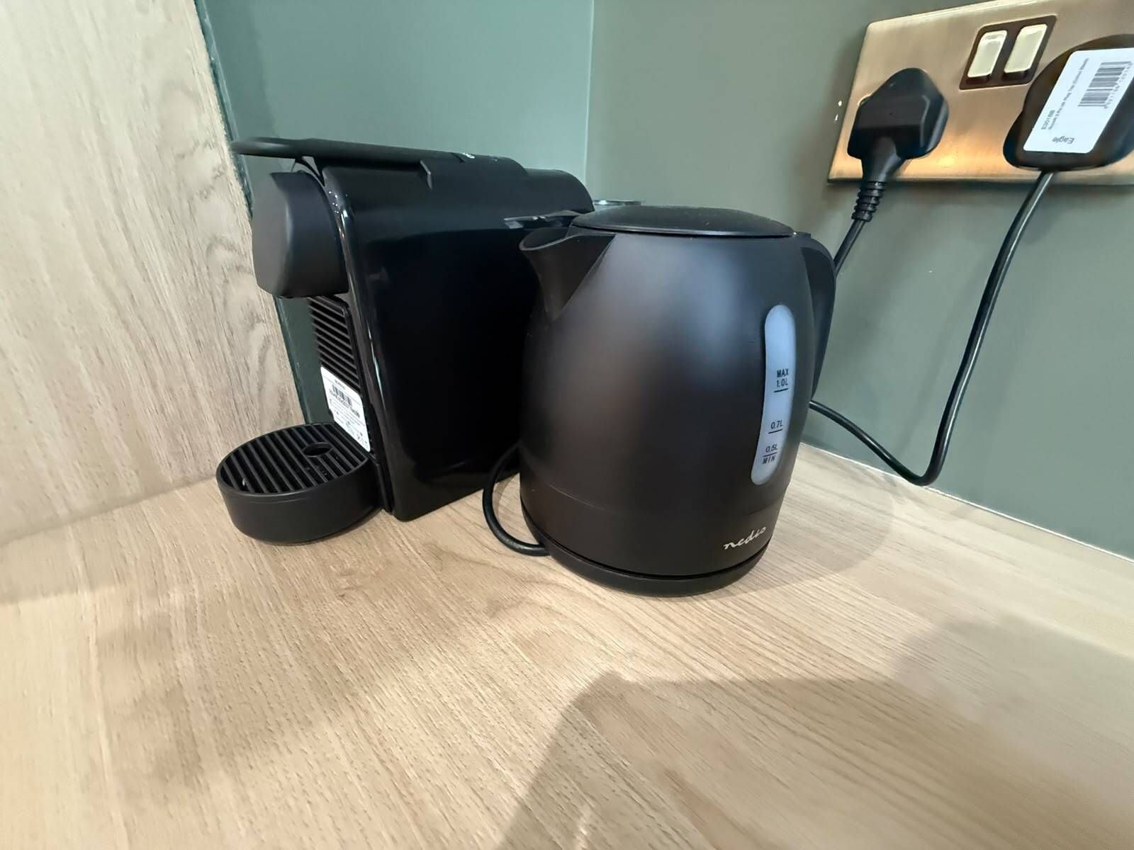 A coffee maker and a kettle on a wooden surface, connected to a power outlet.