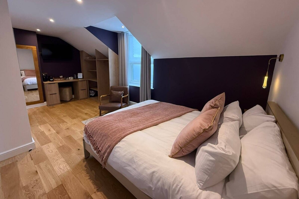 A bedroom with a large bed, a desk, a chair, and a small closet.