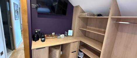 Una habitación compacta con escritorio, barra de café y televisor montado en la pared.