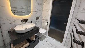 A modern bathroom with a white sink, a mirror with under-cabinet lighting, a toilet, and a shower area. - Auberge (Lytham St. Anne's)