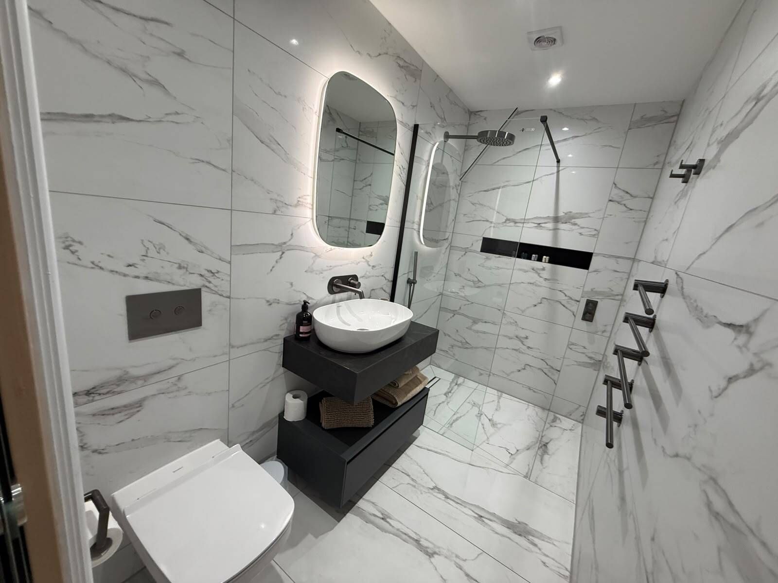 A modern bathroom with a white sink, a mirror, a shower, and marble walls.