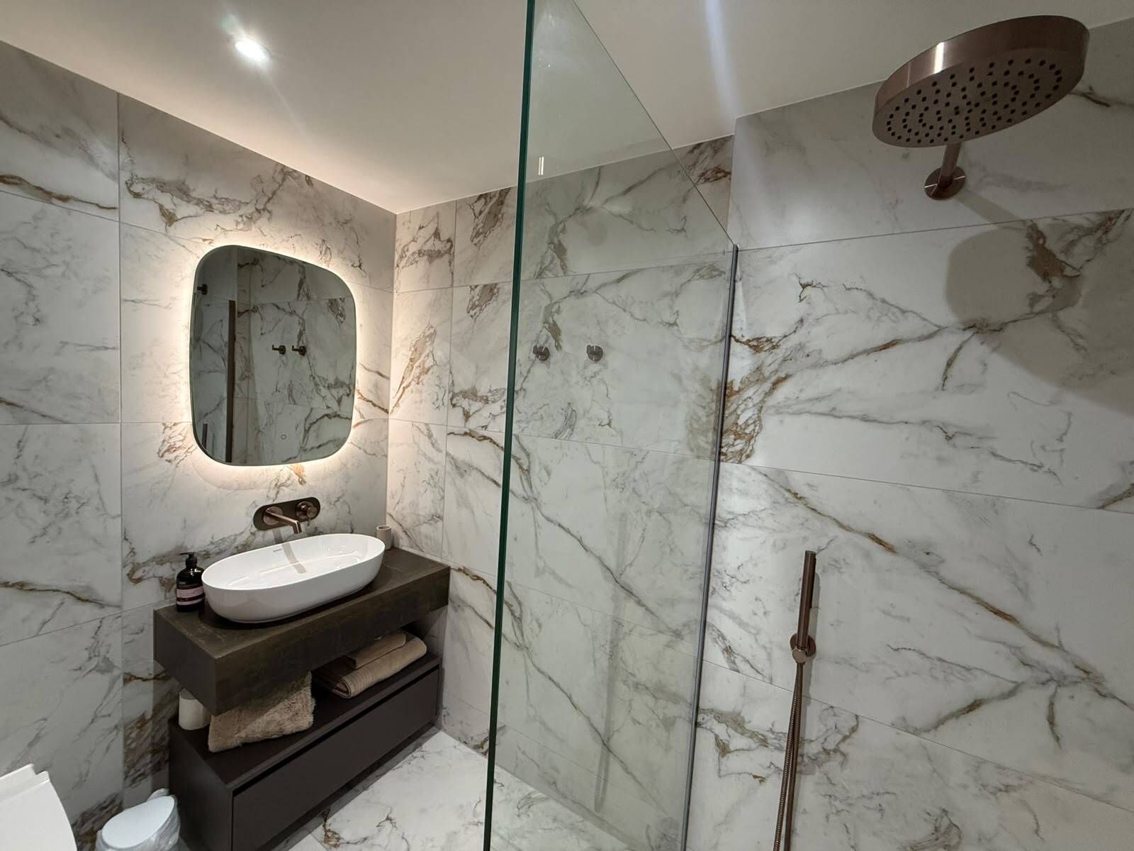 A modern bathroom with a marble vanity, a freestanding bathtub, and a glass-enclosed shower area.