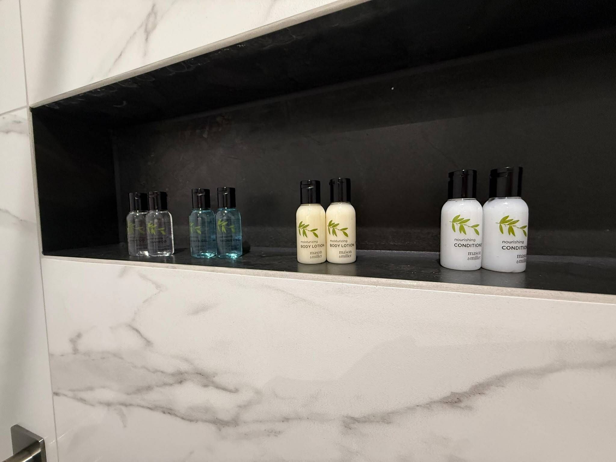 A bathroom shelf with various toiletries including body lotion, body spray, and nourishing conditioner.