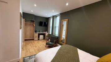 A bedroom with a bed, a desk, a chair, a wardrobe, and a television.