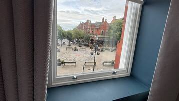 A window with a view of a courtyard with benches, a patterned pavement, and red brick buildings.