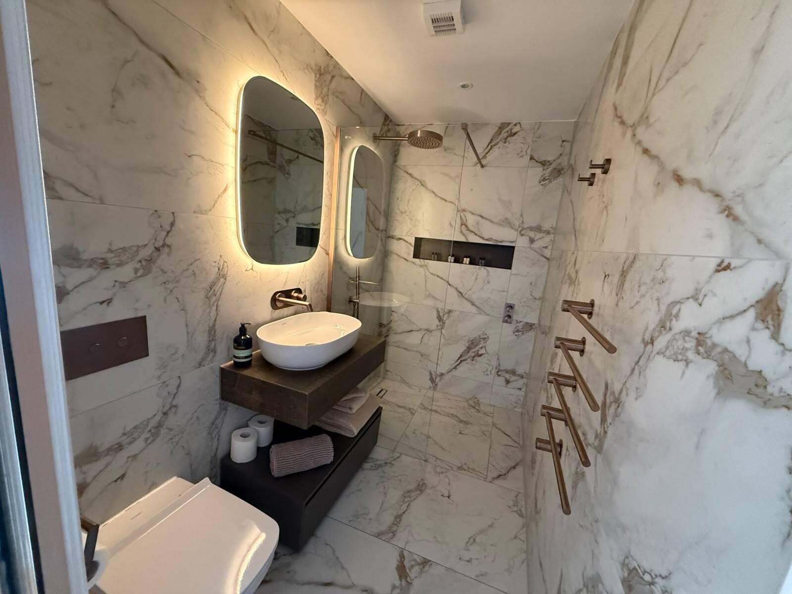 A modern bathroom with a marble sink, two mirrors, a shower, and a toilet.