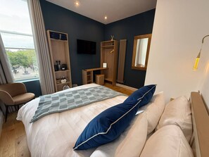 A modern hotel room with a bed, a seating area, a wardrobe, a television, and a window with a view. - Auberge (Lytham St. Anne's)
