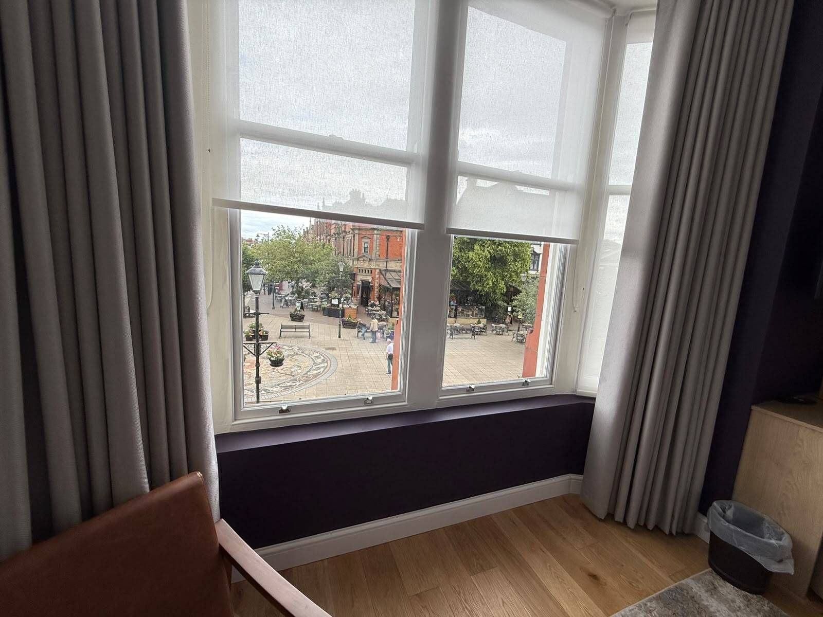 A room with a large window, a wooden floor, and a dark-colored wall.