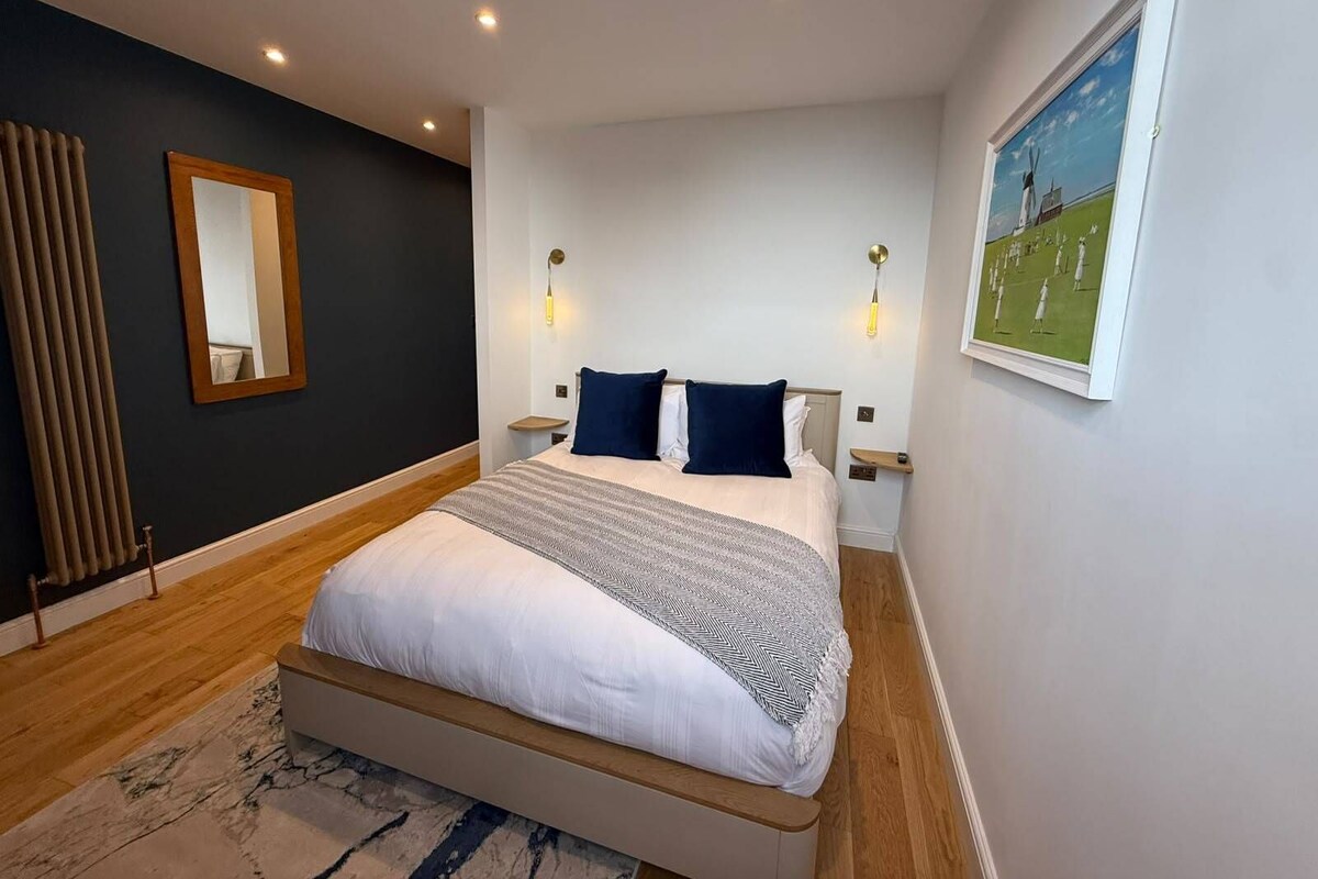 A bedroom with a bed, bedside tables, a mirror, and a painting on the wall.