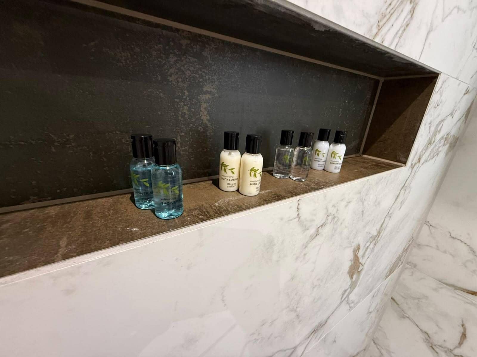 A marble shelf with various toiletries including body lotion and shower gel.