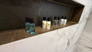 A marble shelf with various toiletries including body lotion and shower gel.