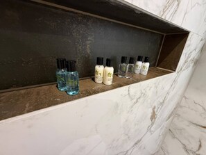 Une étagère en marbre où sont rangés divers produits de toilette, notamment une lotion pour le corps et un gel douche.