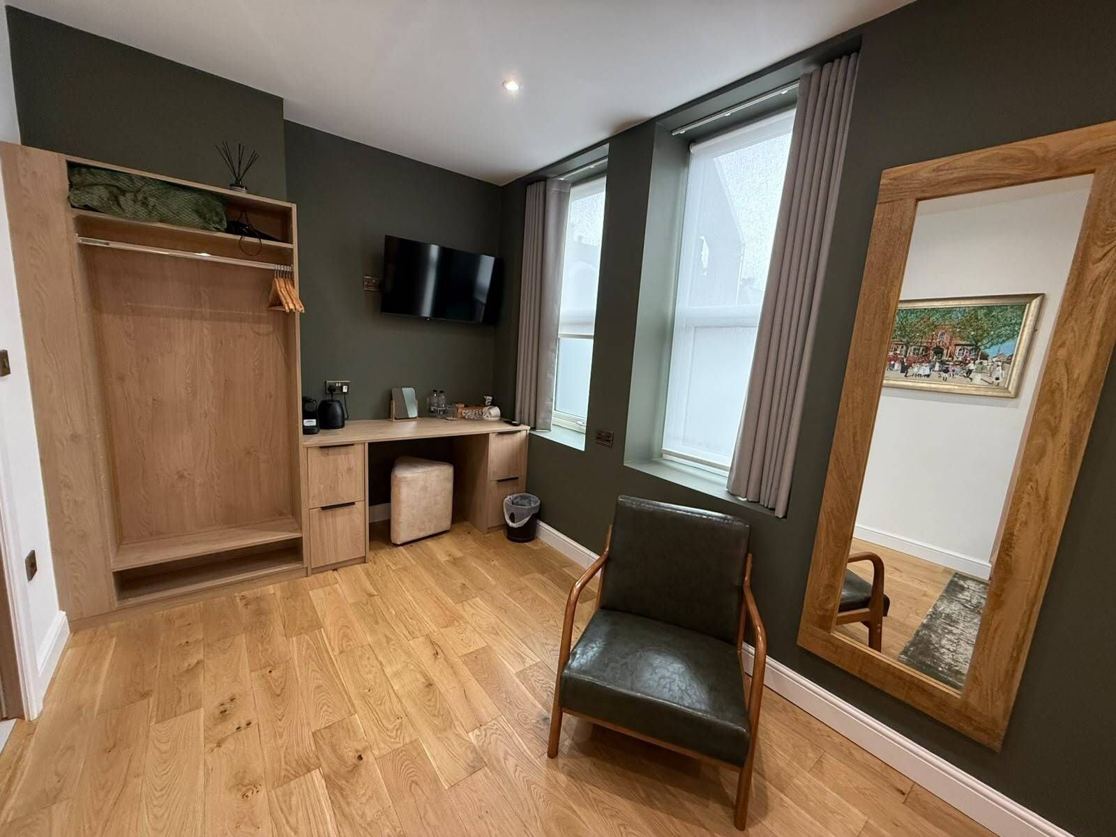 A room with a wooden desk, a chair, a TV mounted on the wall, and a window with curtains.