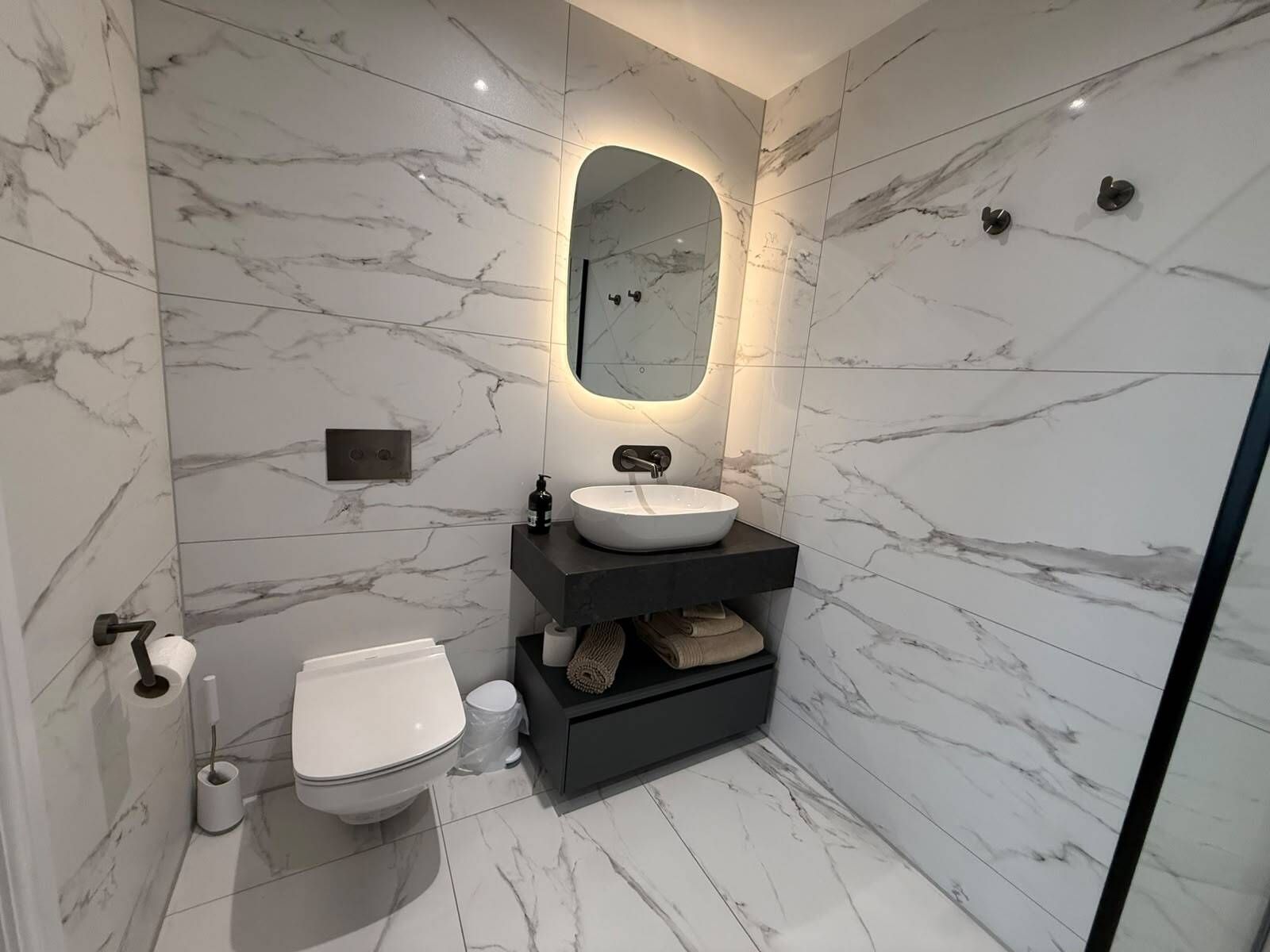 Un bagno moderno con pavimento in marmo, un lavandino bianco, un water e un portasciugamani.