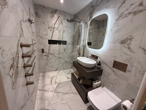 Un baño moderno con piso de mármol, lavamanos independiente, ducha y retrete.