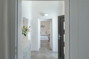 A hallway leading to a bedroom with a bed, a wall-mounted light fixture, and a decorative wall piece. - Aleanna Traditional Villa @ Fira 3-bedroom-3 bathroom (Thera Fira)