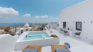 Una azotea con jacuzzi, sillones de descanso y comedor con vistas a un pueblo costero.