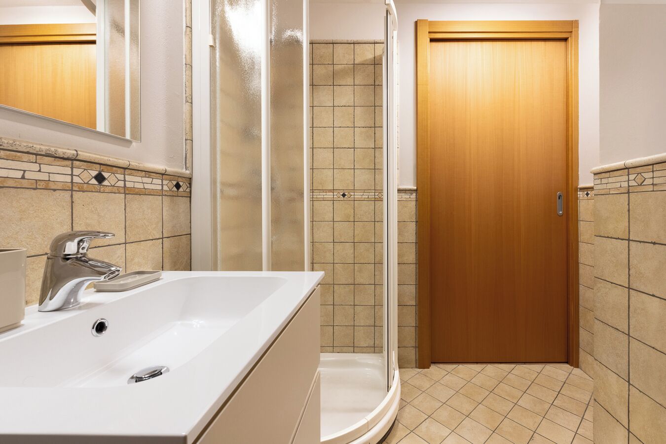 A bathroom with a white sink, a shower enclosure, and a wooden door.