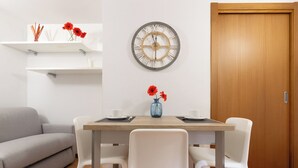 Uma sala de jantar com mesa de madeira, cadeiras brancas, um relógio e uma porta.