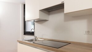 Uma cozinha moderna com uma pia de aço inoxidável, um fogão por indução preto e uma janela acima da pia.