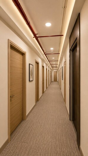 A hotel corridor with doors on both sides, carpeted flooring, and recessed lighting.