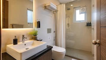 Un baño moderno con un espejo grande, un lavamanos blanco, un inodoro y una zona de ducha con mampara de vidrio.