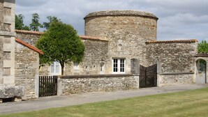 Un bâtiment en pierre doté d’une tour ronde, d’une porte et d’un arbre à l’avant.