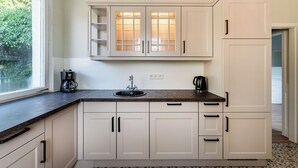 Una cocina con armarios blancos, encimera oscura, cafetera y lavabo.