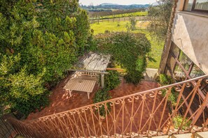 A staircase with ornate metal railings leading to a covered outdoor area with a wooden table and chairs, surrounded by lush greenery and a view of a vineyard. - Alloggio turistico Isola dei Cavalli (Manziana)