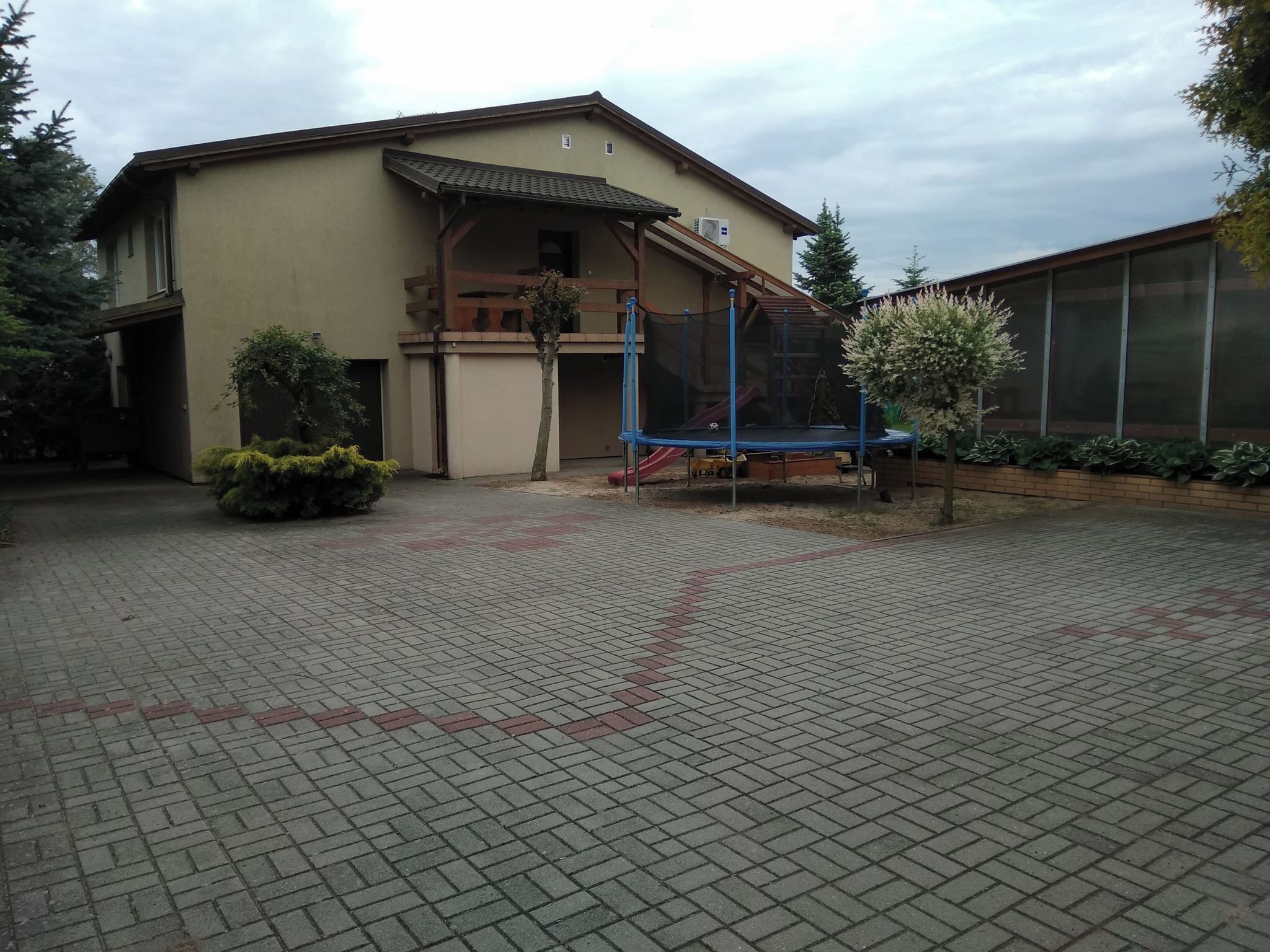 Ein Gebäude mit überdachter Veranda, Trampolin und einem eingezäunten Bereich mit Rutsche.