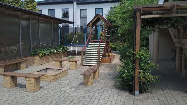 Un'area patio con un'attrezzatura da gioco in legno, panchine e un muro in mattoni.