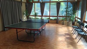 Una sala con ampie finestre, sedie e piante in vaso, con un tavolo da ping pong.
