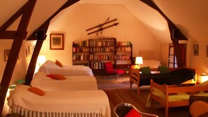 A cozy attic room with two beds, a bookshelf, and a red chair.