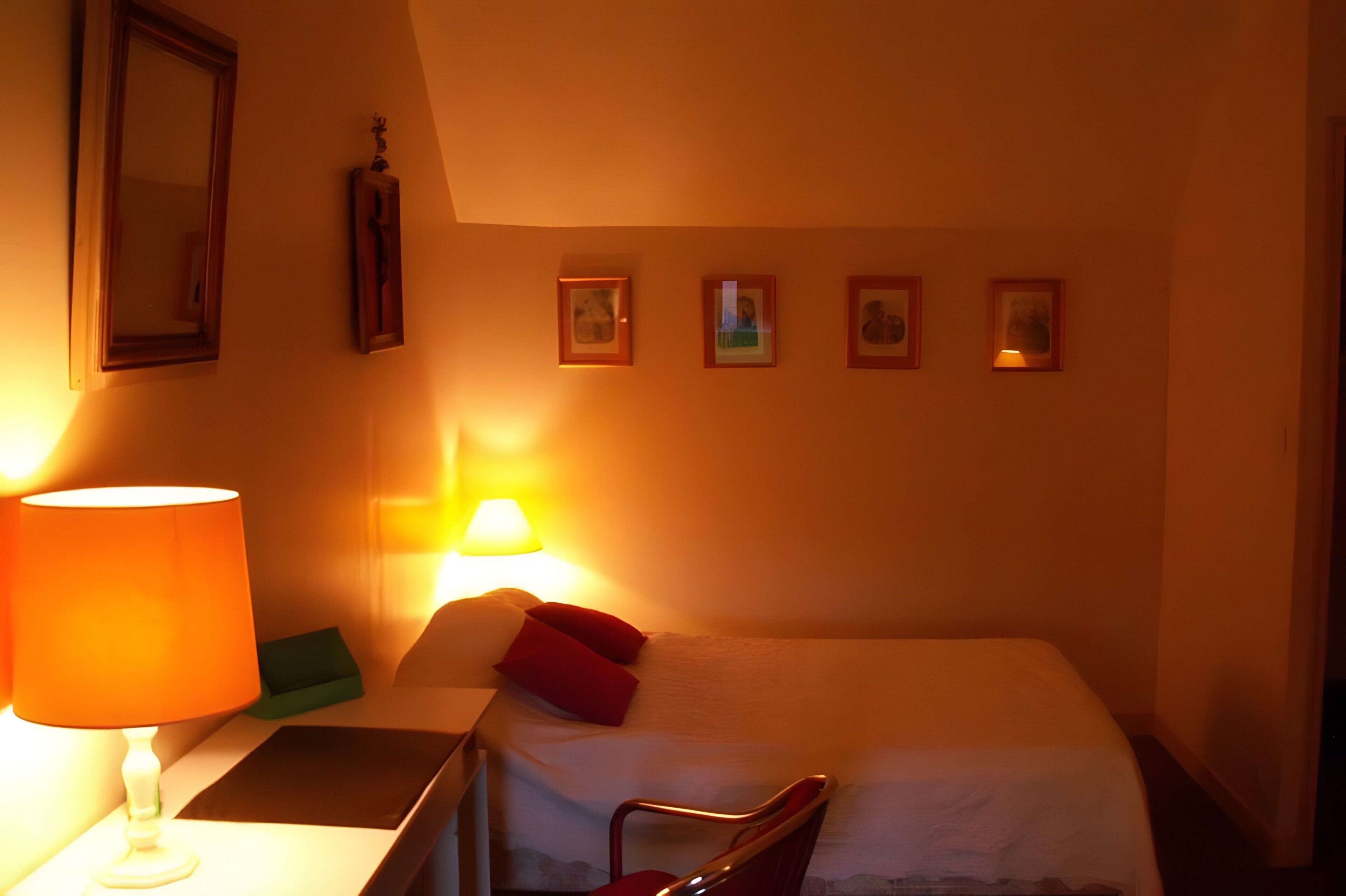 Ein Hotelzimmer mit einem Bett, einem Nachttisch, einer Lampe und vier gerahmten Bildern an der Wand.