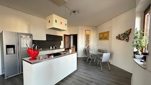 Una cocina moderna con una isla central, un área de comedor con una mesa de vidrio y un espacio de sala con una planta.