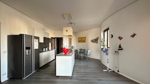 Una cocina moderna con una isla central, un comedor con mesa y sillas, y un pasillo que conduce a un dormitorio.