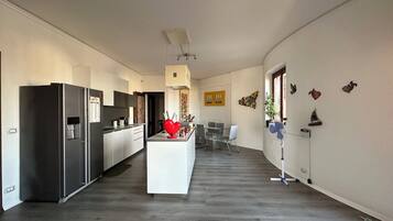 Una cucina moderna con isola centrale, una zona pranzo con tavolo e sedie, e un corridoio che conduce a una camera da letto.