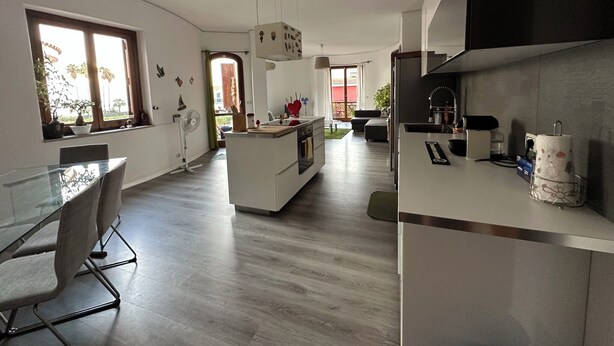 Cocina moderna con una isla central, zona de comedor con mesas de vidrio y vistas al exterior.