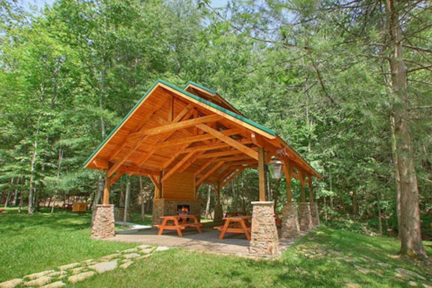 A wooden pavilion with a pitched roof, stone pillars, and picnic tables.