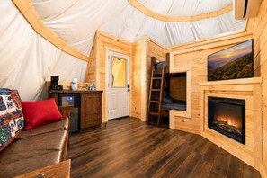 A cozy interior with a wooden floor, a sofa, a fireplace, and a television. - Bear Claw Tepee | Near Dollywood | Resort Access (Sevierville)