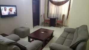 A living room with a TV, two sofas, a coffee table, and a dining table with chairs. - Room-abuja Dannic Hotels - Guest Room (Abuja)